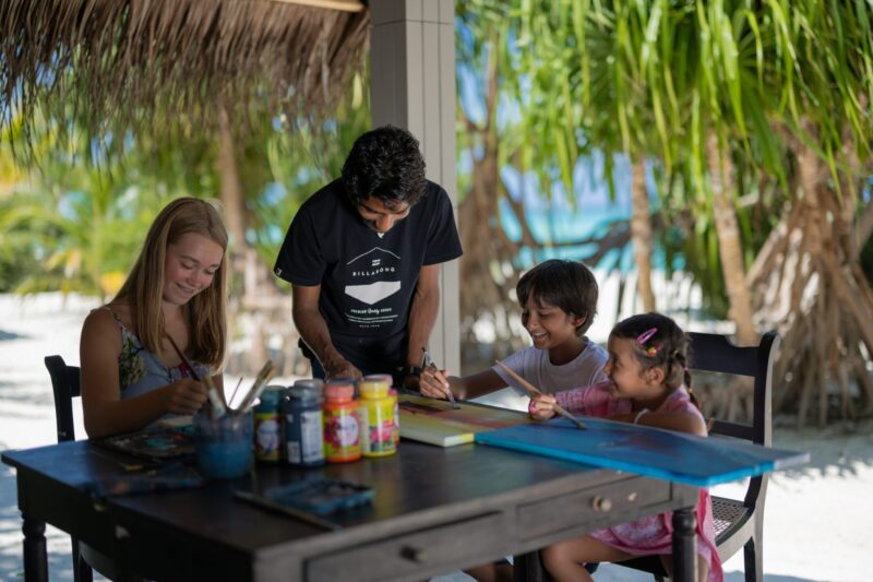 Artistic Fun at CoRa Kids: Group of Kids and Adults Enjoying Painting under a Beach Cottage