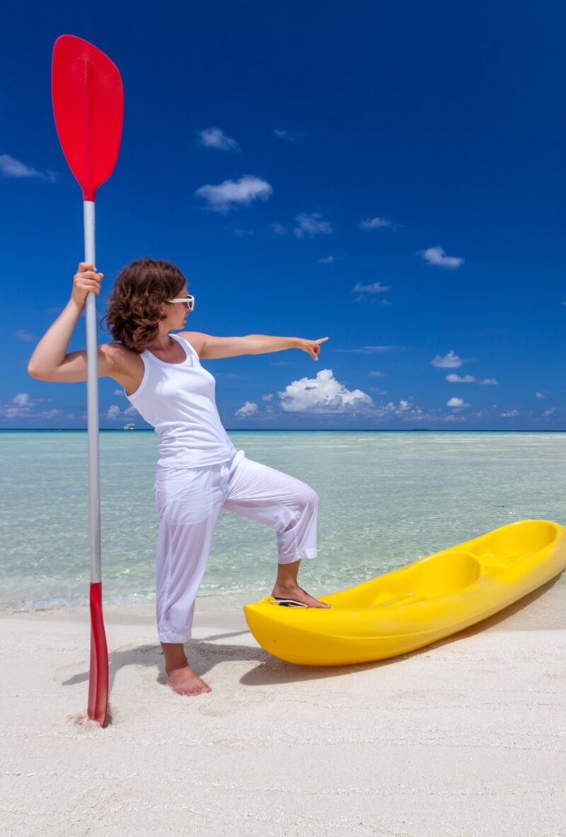 Beach Adventure Ready: Woman Pointing at Ocean, Resting Foot on Kayak with Paddle in Hand